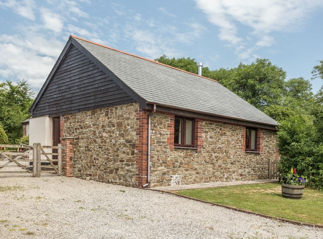 A stone cottage with two windows a wooden gate and a flower pot on the grass at Jenny Wren in Bradworthy