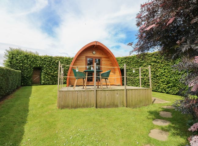 A wooden pod with a deck and table with chairs in a garden surrounded by hedges at Lovesome Pod in Lovesome Hill near Northallerton