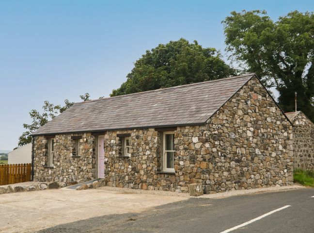A stone cottage with a gray roof and a pink door next to a paved road at Old Shop Cottage in Limavady