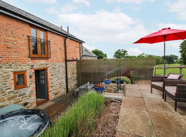 An outdoor space with a hot tub and seating at Meadow Barn in Aston On Clun