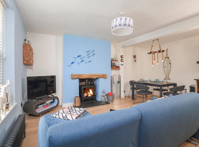 A living room with a blue couch facing a wood stove in a blue fireplace and a dining table with chairs at 25 Lake Street in Dartmouth