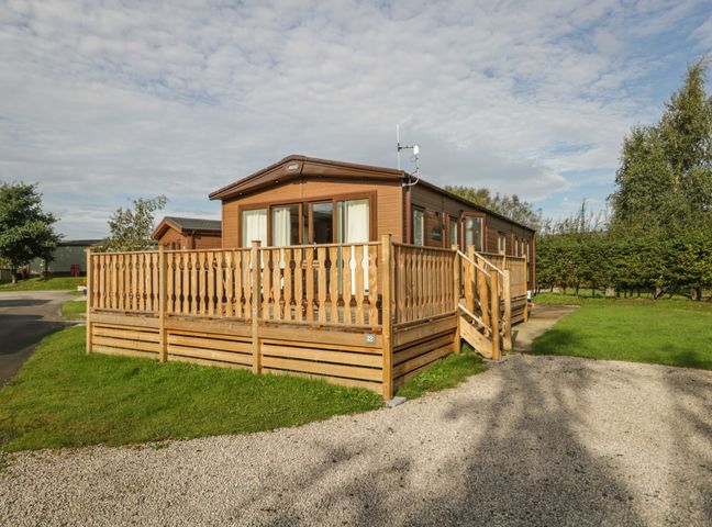 A wooden mobile home with a fenced deck and a gravel driveway at 22 Sherwood South Lakeland Leisure Village near Warton