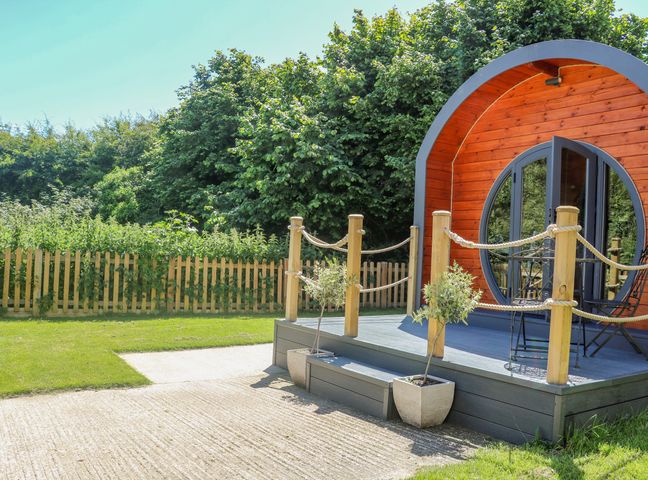 A circular wooden pod with a small porch and potted plants surrounded by a fenced garden at Filbert Pod in Arundel West Sussex