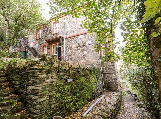 Stone building with external staircase next to stone wall and pathway surrounded by trees at Lewarne in Boscastle