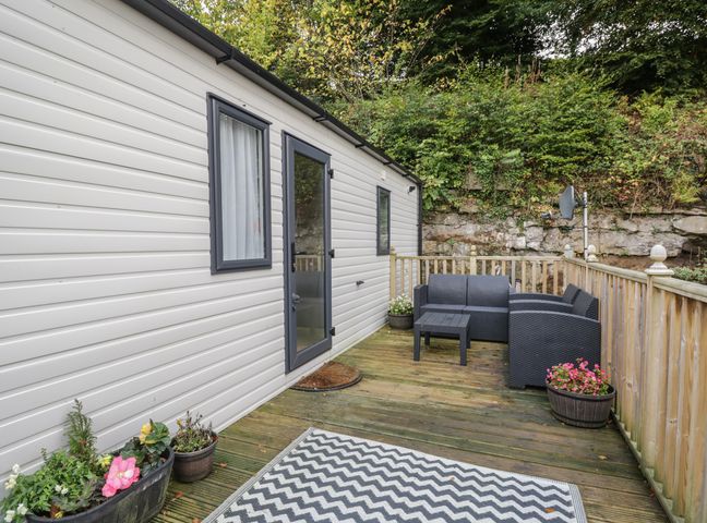 An outdoor deck with black patio furniture and potted plants next to a white building at Burlees Nest in Brigham near Great Broughton Cockermouth