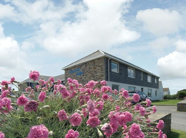 A cluster of pink flowers with a two-story building and parked car in the background at Polzeath Court 4 in Polzeath