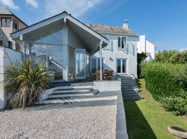 Exterior view of a white house with large windows patio stairs gravel area and garden at Signal Post in Port Isaac