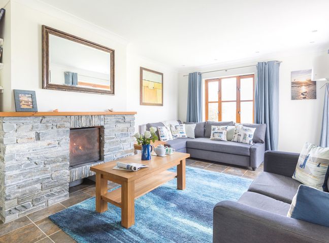 A living room with two grey sofas a blue rug a wooden coffee table and a stone fireplace at Lundy Cottage in Rock