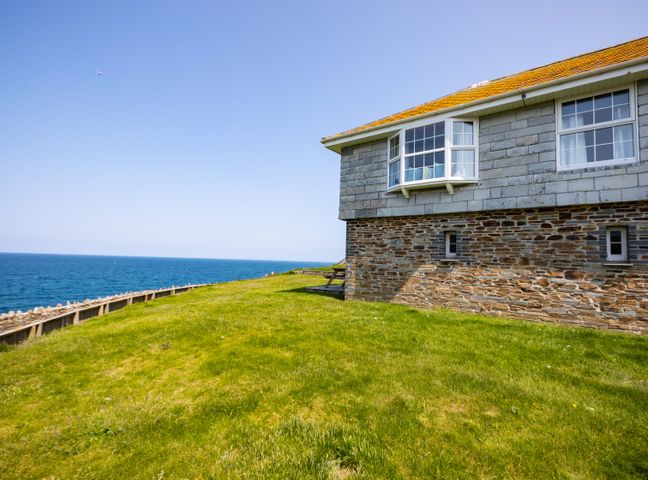 A stone house with windows on a grassy cliff overlooking the sea at Gulland in Port Isaac