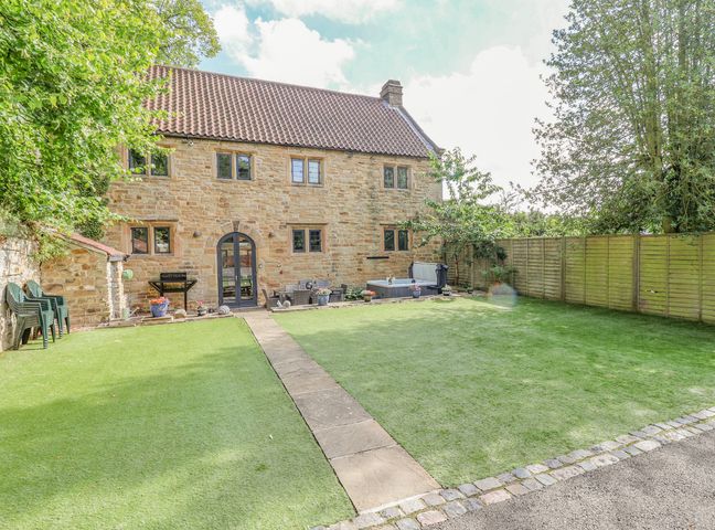 A stone house with a tiled roof and a garden with potted plants and outdoor furniture at The Gatehouse in Mansfield