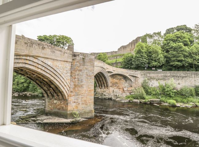 A stone bridge over a river with trees and ruins in the background at 1 The Riverside in Barnard Castle