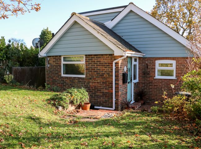 A small brick house with blue siding and white trim surrounded by a lawn and trees at Cosy Cottage in Bexhill-On-Sea