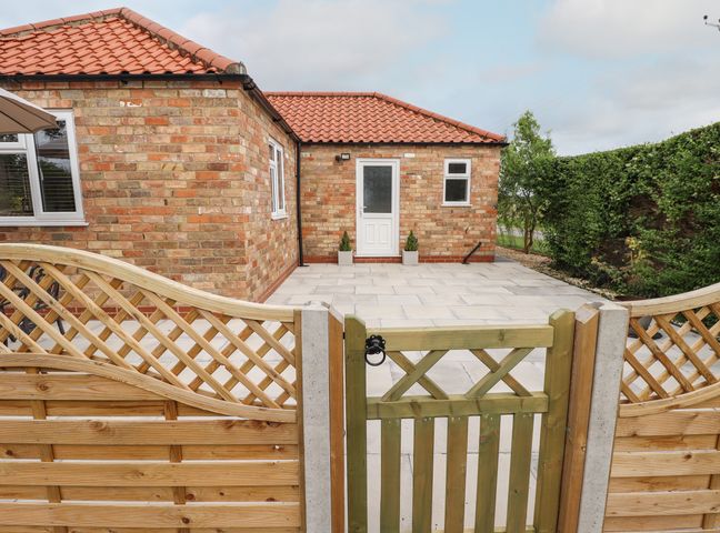 A brick house with a tiled roof and patio behind a wooden gate and fence at The New Build in South Reston near Louth