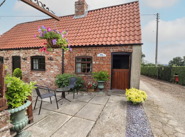 A brick cottage with a tiled roof a wooden door potted plants outdoor chairs and table on a paved patio at Woldsend Cottage in Horncastle