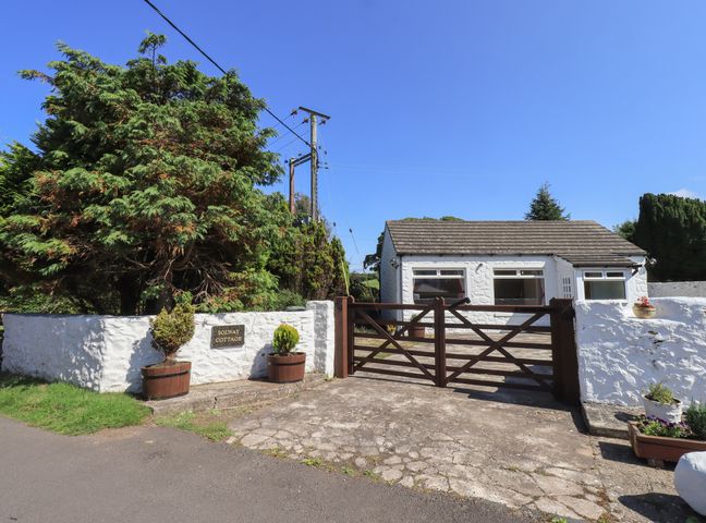 A white stone cottage with a gated driveway and large trees behind a white wall at Solway Cottage Powfoot near Annan