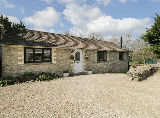 A stone cottage with a tiled roof gravel driveway and potted plants at Orchard House Cottage in Malmesbury