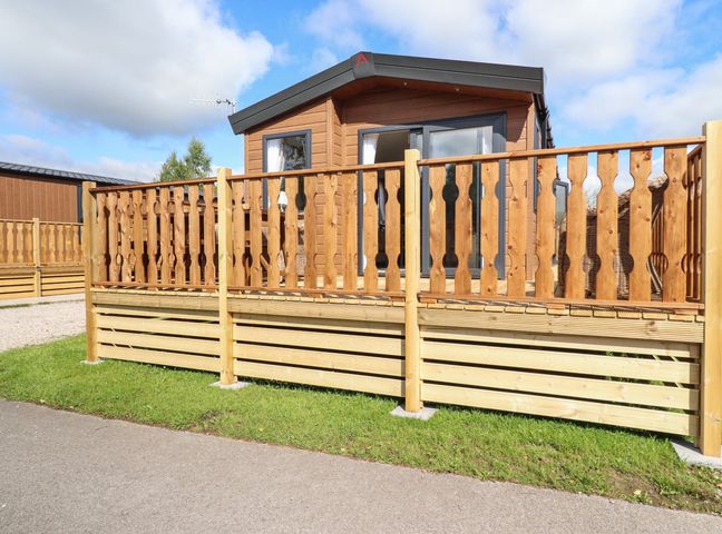 A wooden cabin with a fenced wooden deck and grassy area at 25 Sherwood in South Lakeland Leisure Village