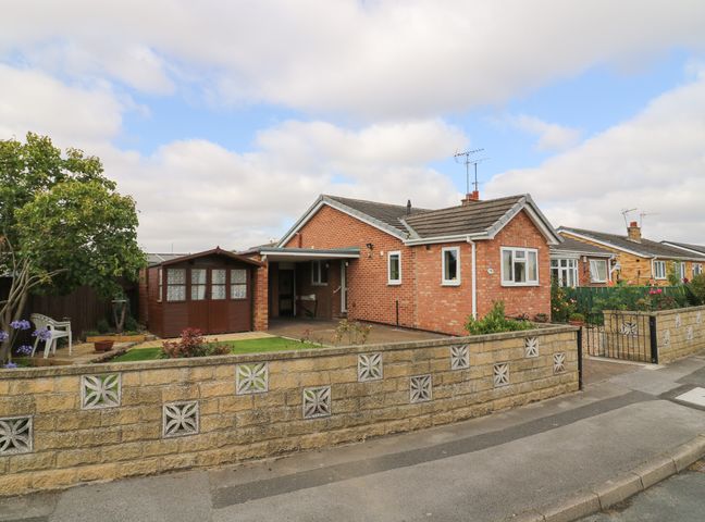 A brick bungalow with a garden shed a small lawn and a tree behind a low stone wall at The Corner Bungalow in Driffield