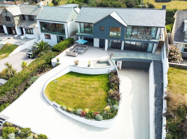 A modern two-story house with a grass lawn and outdoor seating area at Megizzy in Polzeath
