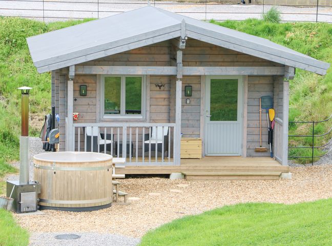 A small wooden cabin with a porch and hot tub outside at Otters Holt in Winston near Staindrop