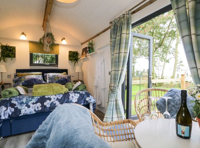 A bedroom with a double bed and floral bedding next to a table with two chairs by a glass door at High Rigg Shepherd's Sunset in Brampton Cumbria