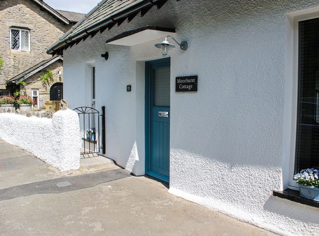 The entrance of a white cottage with a blue door and a black sign reading Moorhurst Cottage in Kents Bank near Grange Over Sands