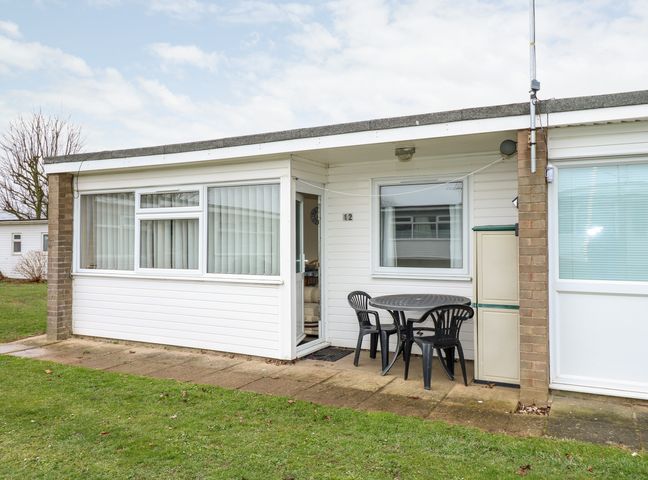 A patio with a round table and three chairs outside a white building at Chalet 12 in Hemsby