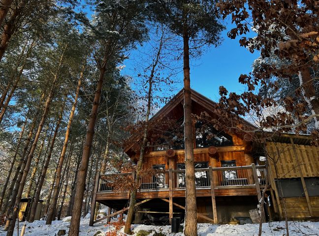 A wooden cabin with a deck among snow-covered trees under a blue sky at Pine Marten Lodge in Dulnain Bridge near Nethy Bridge