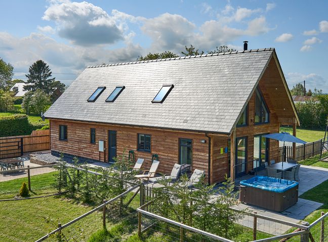 A wooden house with a patio featuring a hot tub chairs and a dining table with an umbrella at Holly Lodge in Forden near Montgomery