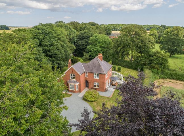 A red brick house with a slate roof surrounded by trees and grass at Routhorpe House in Bainton near Great Driffield