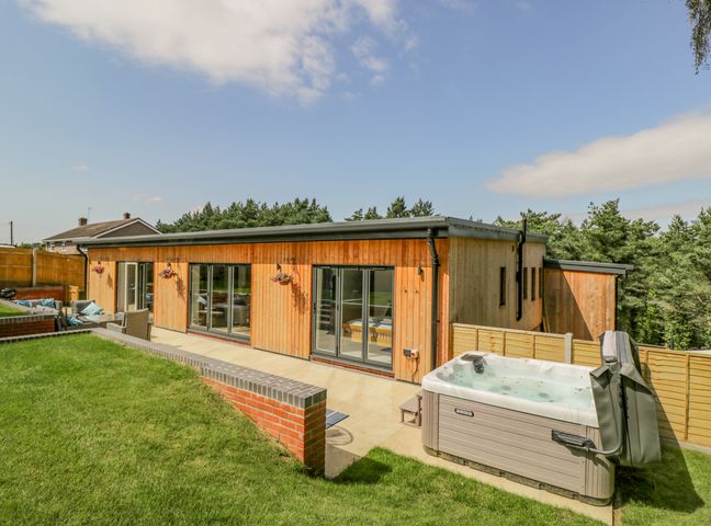 A wooden house with large glass doors a hot tub a lawn and a patio area at The Barn in Lytchett Matravers