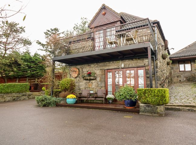 A stone building with balcony and outdoor seating area with plants and flower pots at The Bothy in Cammachmore near Newtonhill