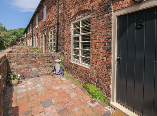 A brick patio with potted flowers and a black door numbered 8 at Number 7 in Ironbridge