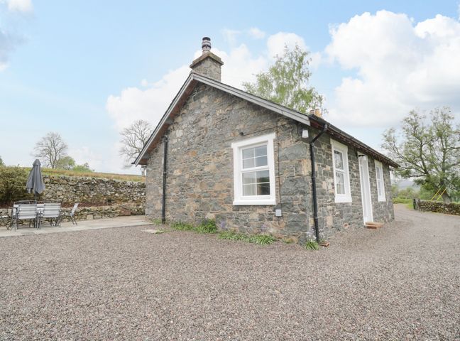 A stone cottage with white framed windows and a gravel yard with outdoor dining furniture at Collieston Cottage in Dunscore near Dumfries