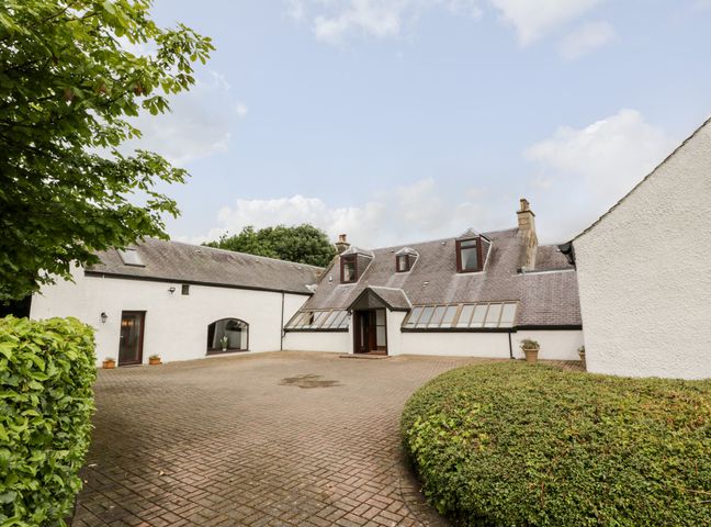 A paved courtyard area with trimmed bushes and a white building with sloped roofs and dormer windows at Shieldhill Farm House in Falkirk