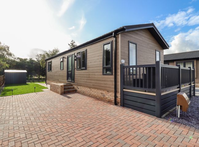 A single-story prefab house with a small porch and paved driveway at Lodge 47 in Buildwas