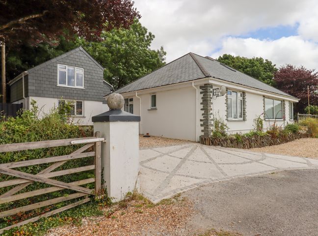 A driveway with a wooden gate and two houses with gray roofs surrounded by trees at Hurdwick Lodge in Tavistock