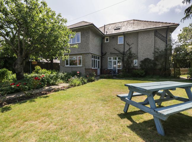 A garden with a tree a flower bed and a wooden picnic table outside a two story house at Molly's Place in Boscombe