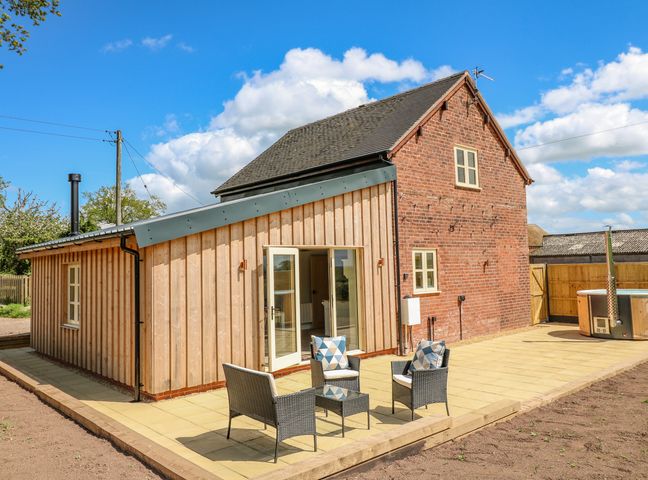 A patio with outdoor seating and a hot tub next to a house with wooden and brick walls at Acorn Lodge in Sandon Staffordshire