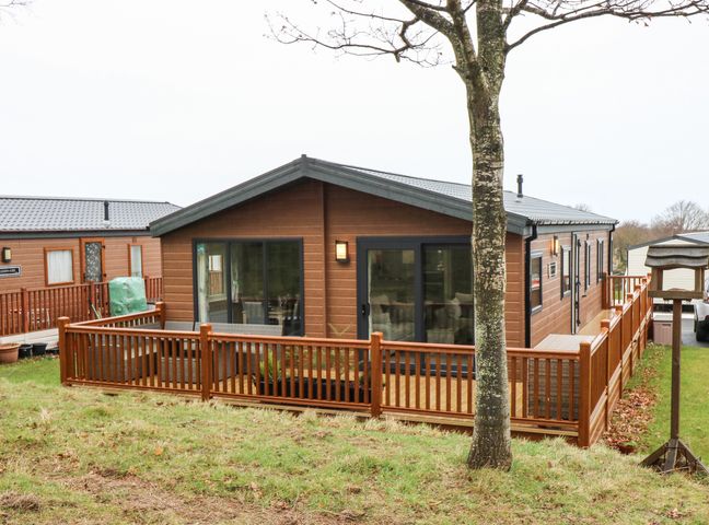 A wooden lodge with large sliding glass doors and a fenced wooden deck in a grassy area at Woodpecker Lodge in Dunbar