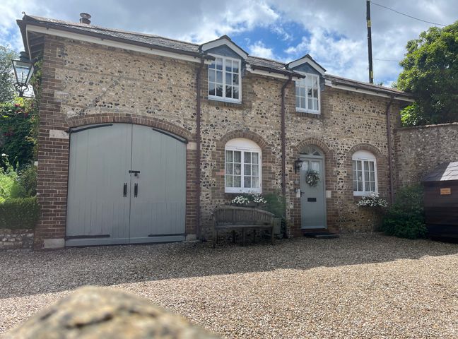 A stone and brick house with arched windows a green door a bench and gravel driveway at The Coach House at Lackington Farm in Piddletrenthide