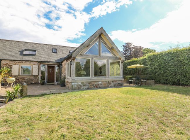 A stone house with large triangular windows and a garden with patio furniture and umbrella at Swallows Barn in Walton near Chesterfield