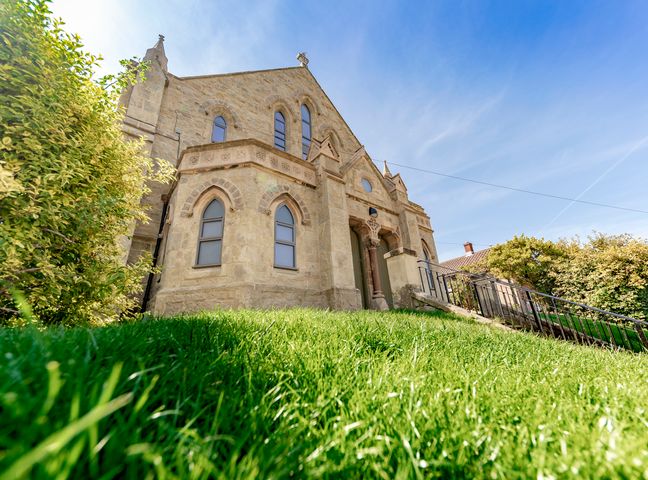 A stone building with arched windows and a staircase with a railing on a grassy hill at Bishops Retreat in Ventnor