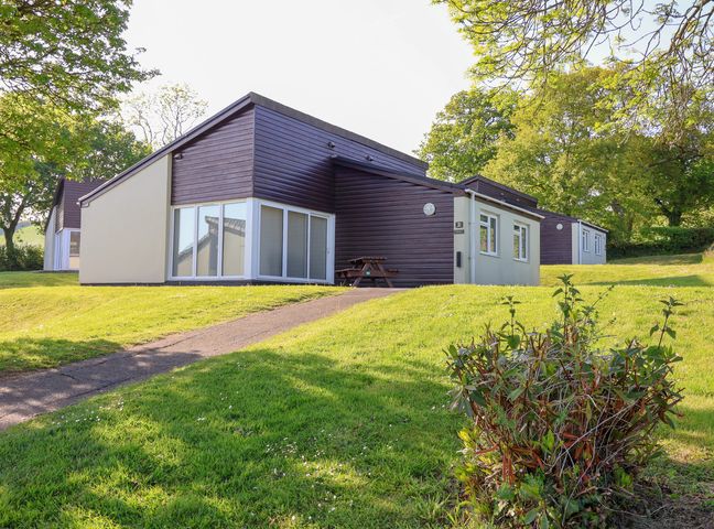 A bungalow with patio doors and picnic table on a grassy hill with trees in the background at Harcombe House Bungalow 2 in Chudleigh