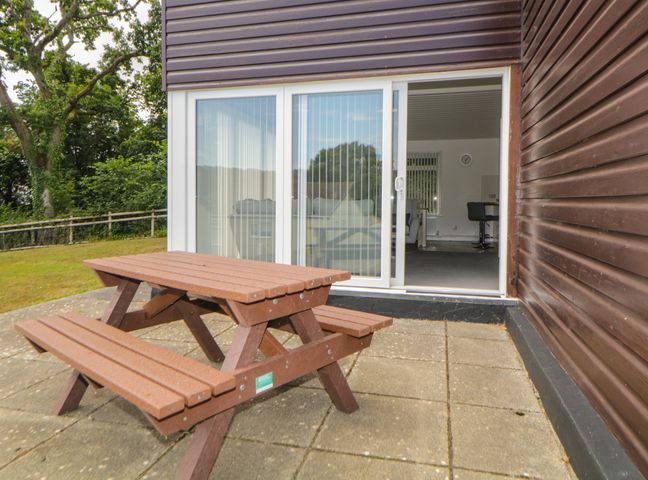A wooden picnic table on a patio outside sliding glass doors of a brown building at Harcombe House  Bungalow 4 in Chudleigh