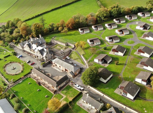 An aerial view of a large building complex with multiple small bungalows and pathways surrounded by green fields at Harcombe House  Bungalow 4 in Chudleigh