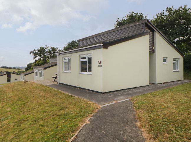 A row of single-story bungalows with paved pathways and grassy areas at Harcombe House Bungalow 6 in Chudleigh