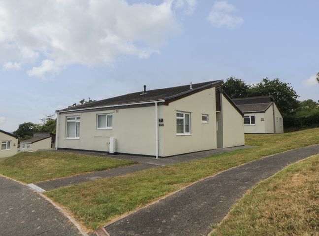 A group of single-story houses with grass and paved paths in front at Harcombe House Bungalow 7 in Chudleigh
