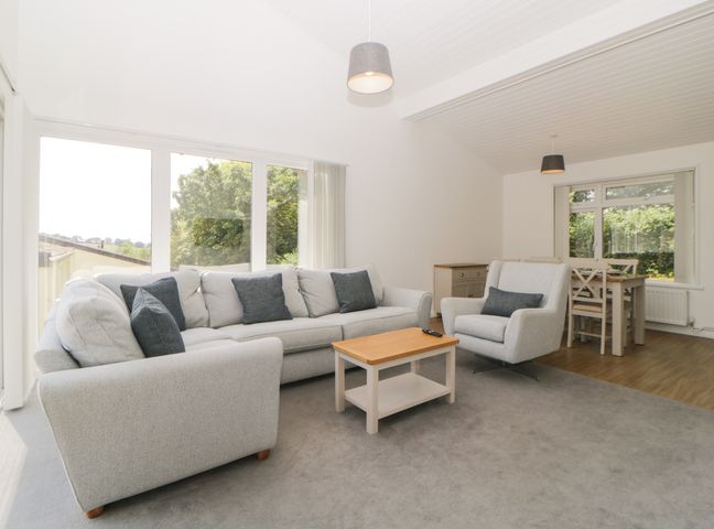 A living room with a gray sofa and armchair surrounding a wooden coffee table next to a dining table at Harcombe House Bungalow 8 in Chudleigh