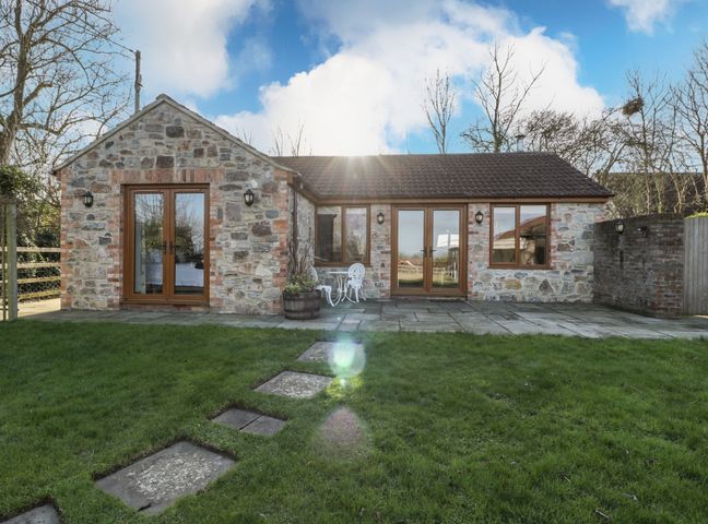 A stone house with wooden doors and windows on a grass lawn with a stone path at The Hide in Edington near Street